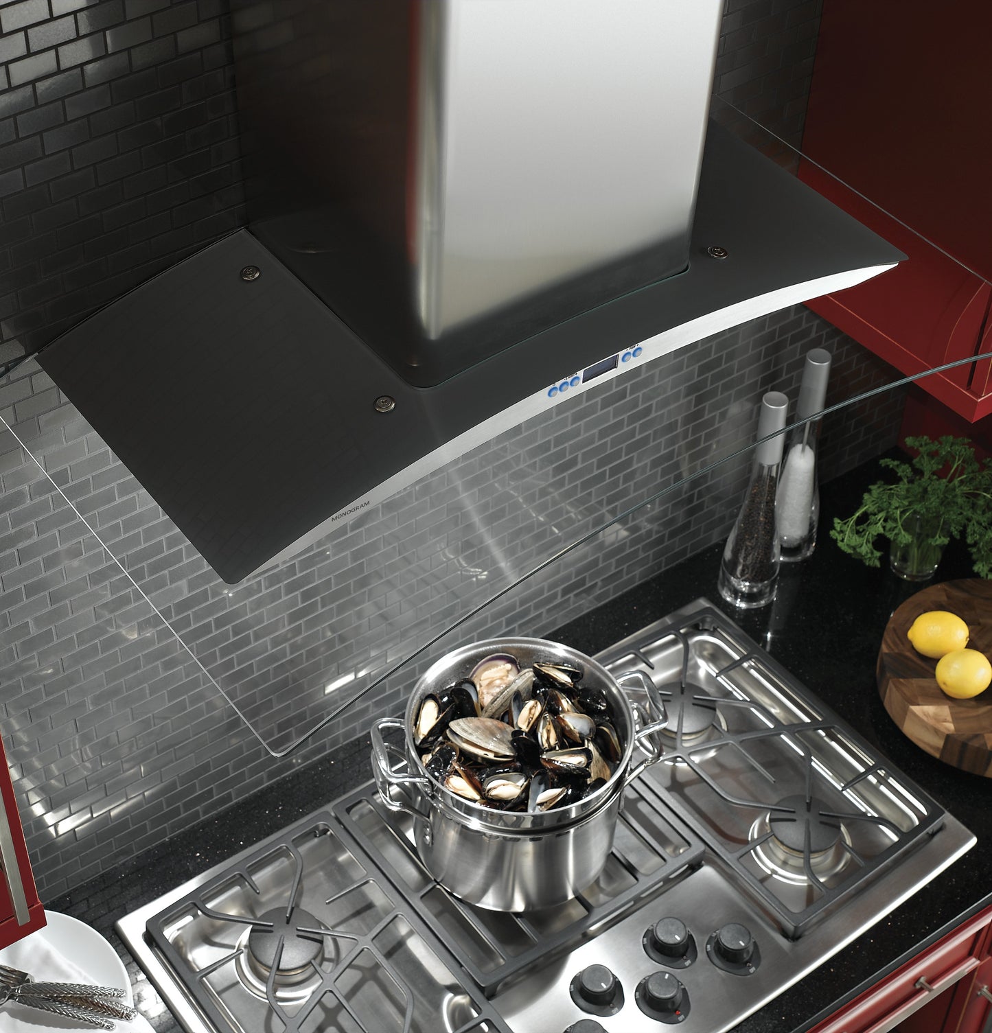Stainless steel and glass canopy wall-mounted range hood over gas cooktop with pot of mussels in kitchen setting