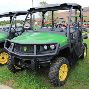 Green full-size John Deere utility vehicle with brush guard, rugged tires, and protective roof for outdoor use
