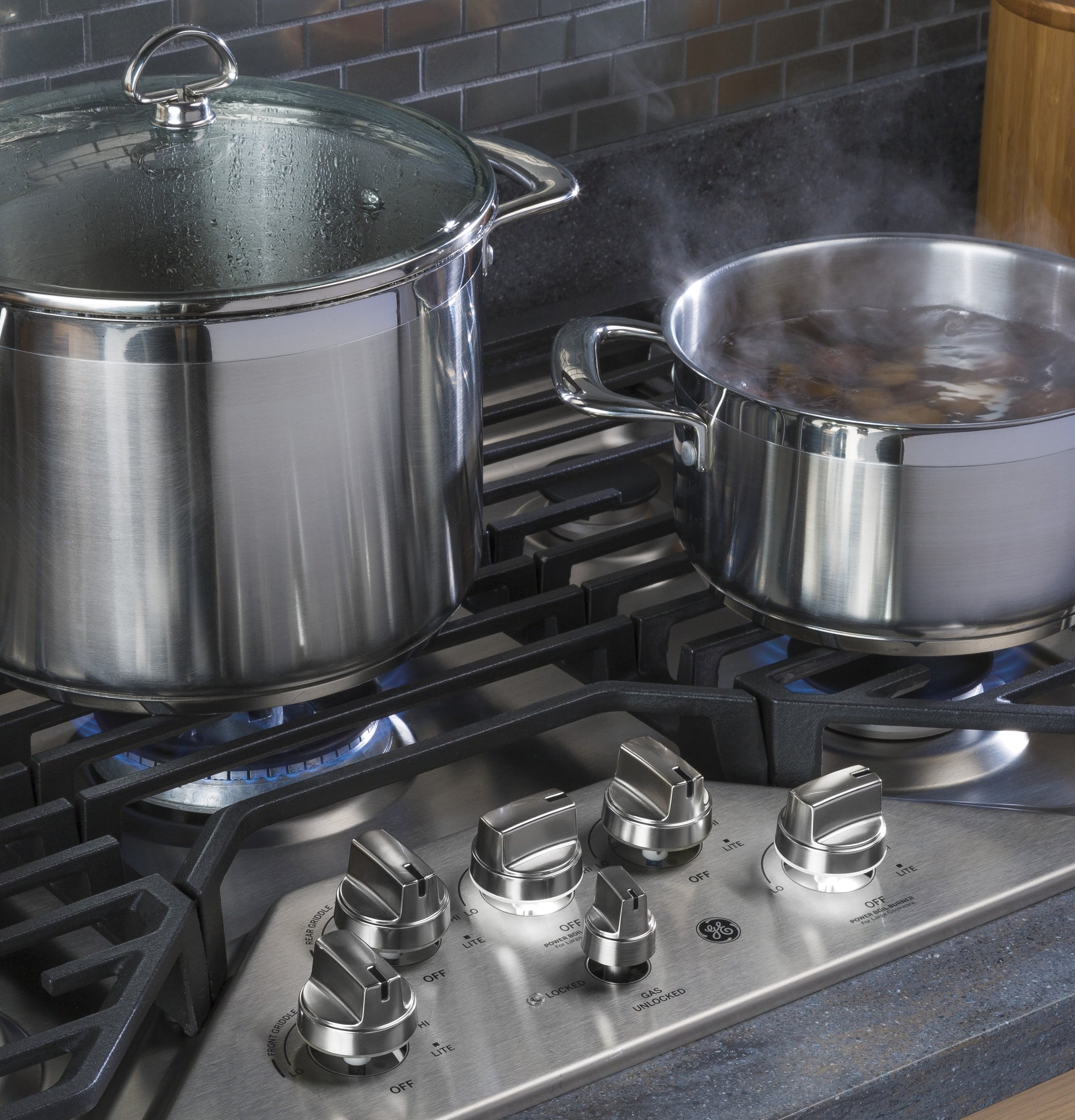 Stainless steel cooktop with five burners featuring heavy-duty grates and control knobs, two pots cooking on blue flames