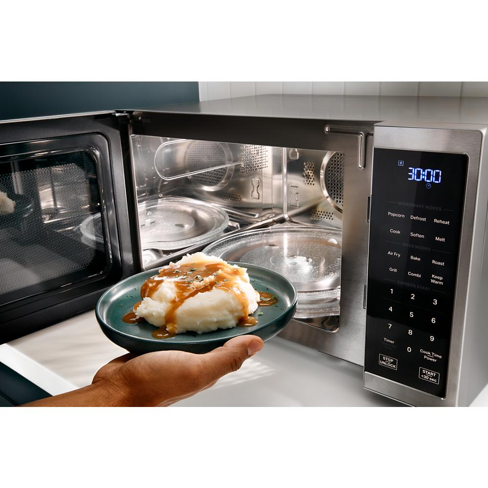 Modern stainless steel countertop microwave with digital display and touch controls next to plate of mashed potatoes with gravy
