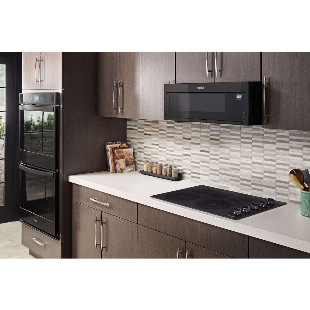 Black low profile microwave hood combination installed above electric cooktop in kitchen with dark wood cabinets and tile backsplash
