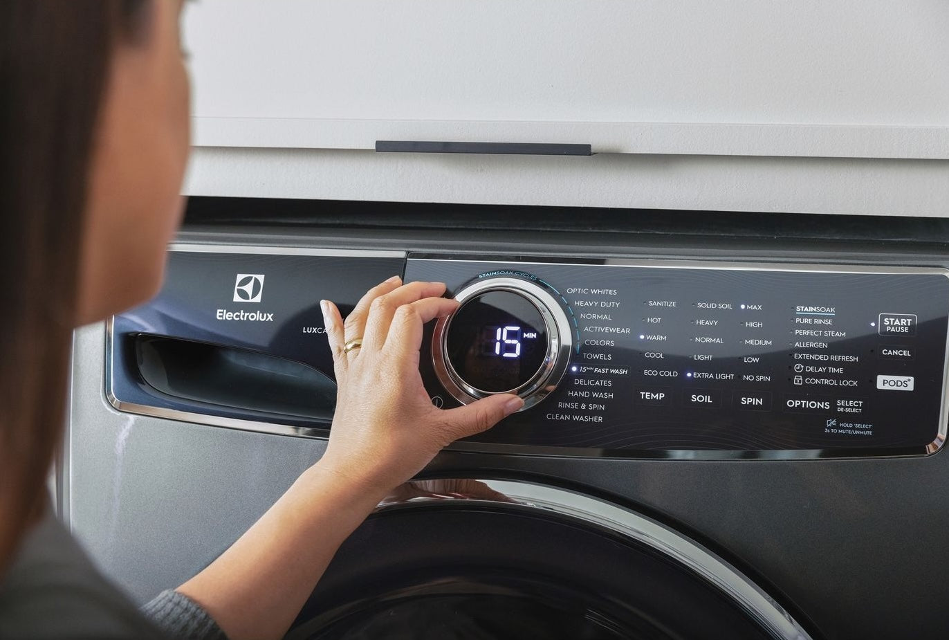 User adjusting dial on a stainless steel Electrolux front load washer control panel in home appliance setting