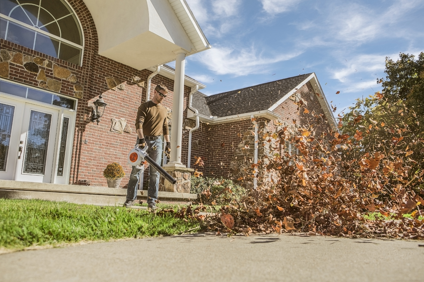 Man using a lightweight gas-powered blower to clear leaves from a residential driveway in a home improvement setting