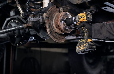 Yellow and black cordless impact wrench with hog ring being used for automotive repair on a vehicle axle assembly