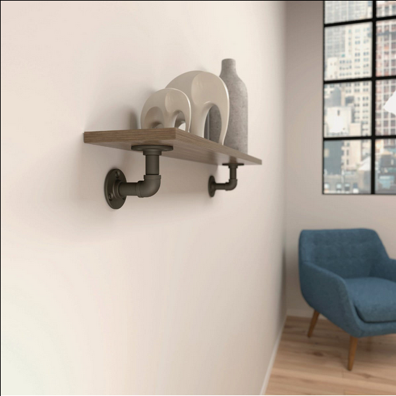 Industrial style elbow pipe bracket in matte black supporting a wooden wall shelf with decorative items for home improvement