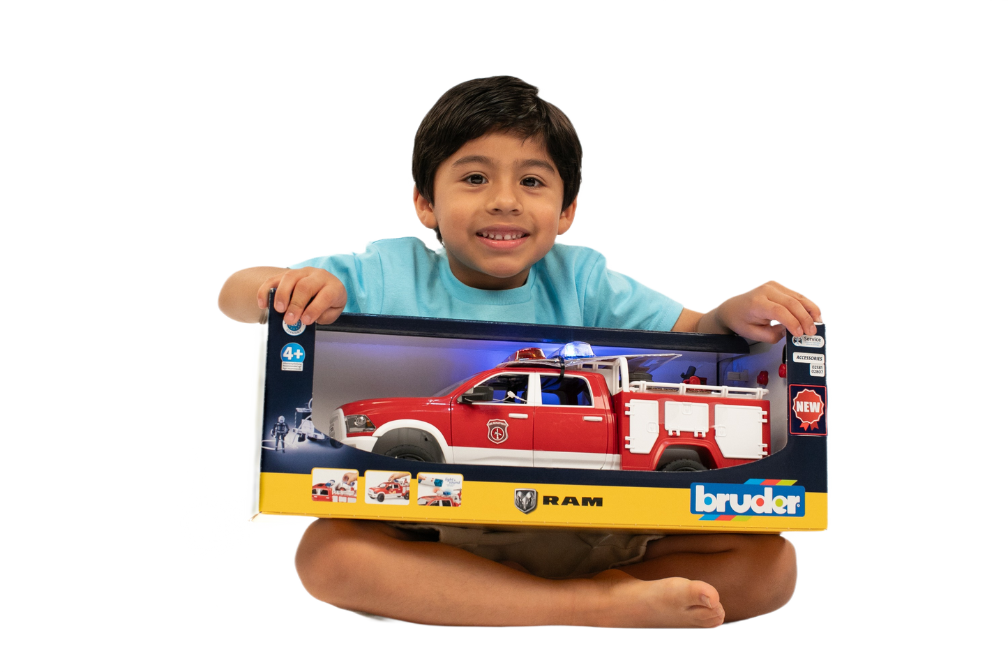 Child smiling while holding boxed Bruder RAM Fire Rescue Truck with light and sound features in colorful packaging