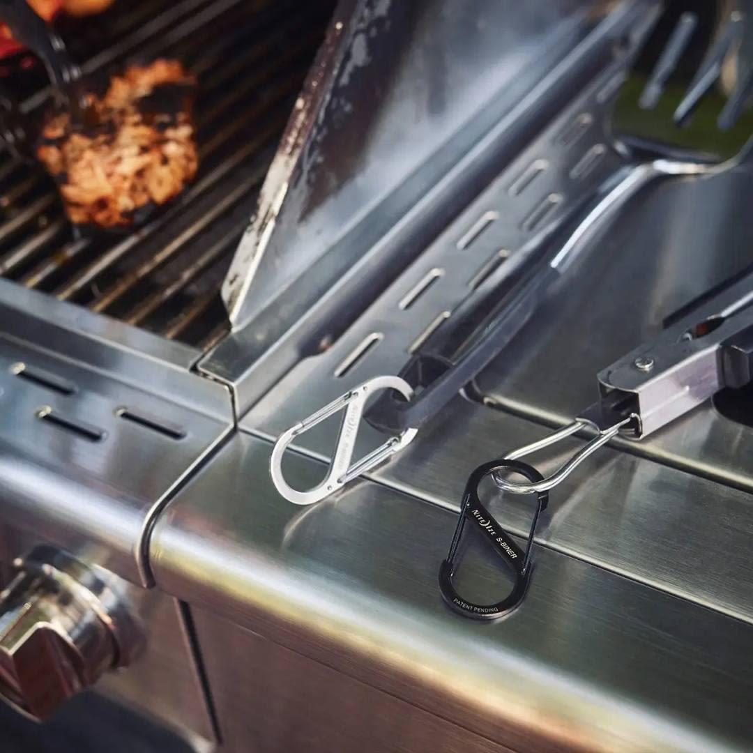 Two stainless steel dual-gated carabiners clipped to a grill side shelf in home improvement hardware collections under $50