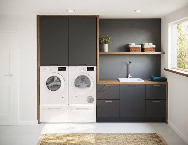 White front load compact washer and dryer paired within black and wood cabinetry next to a laundry sink in modern utility room