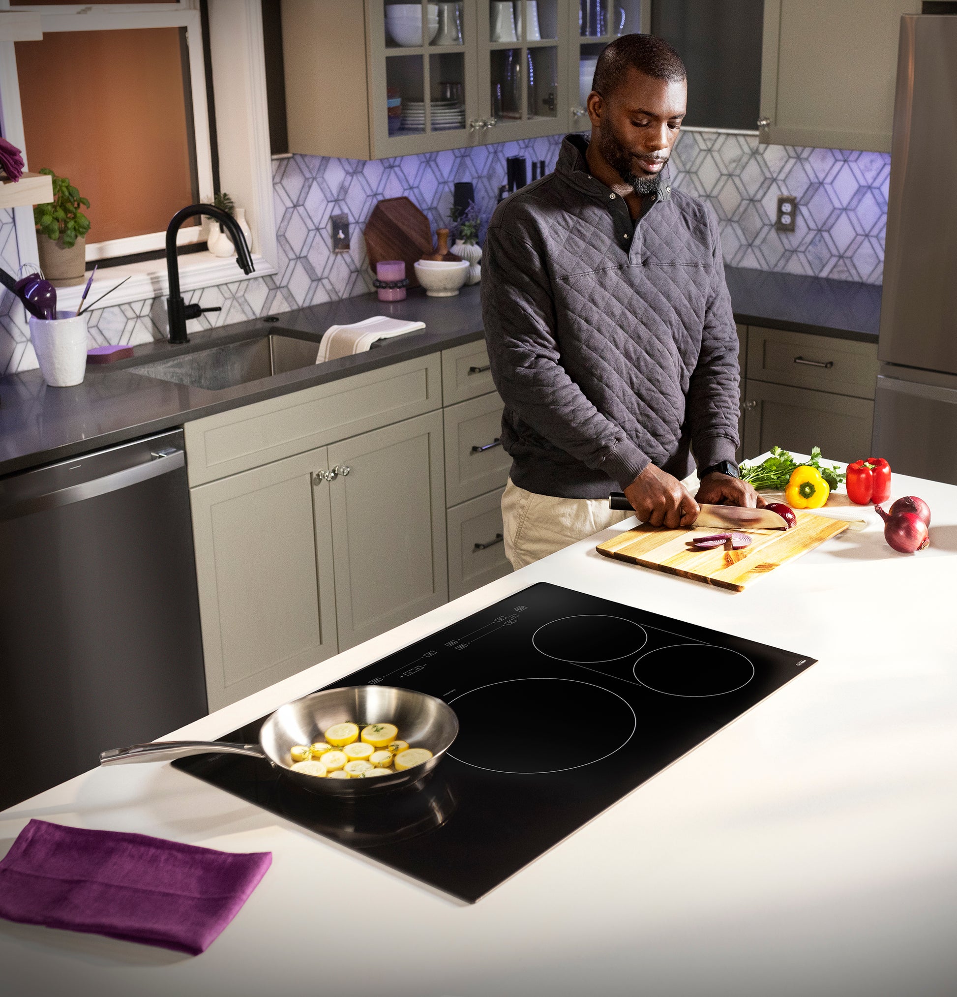 Modern kitchen with black built-in induction cooktop cooking sliced squash in stainless steel pan on white island countertop