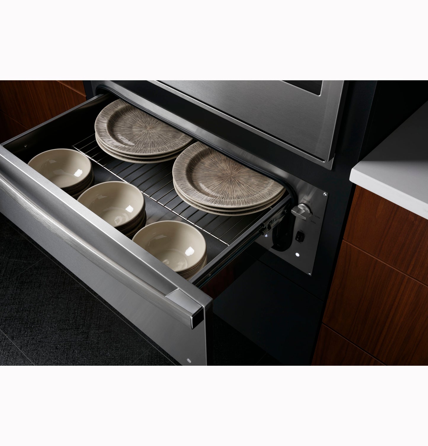 Open stainless steel warming drawer holding ceramic plates and bowls in contemporary kitchen setting