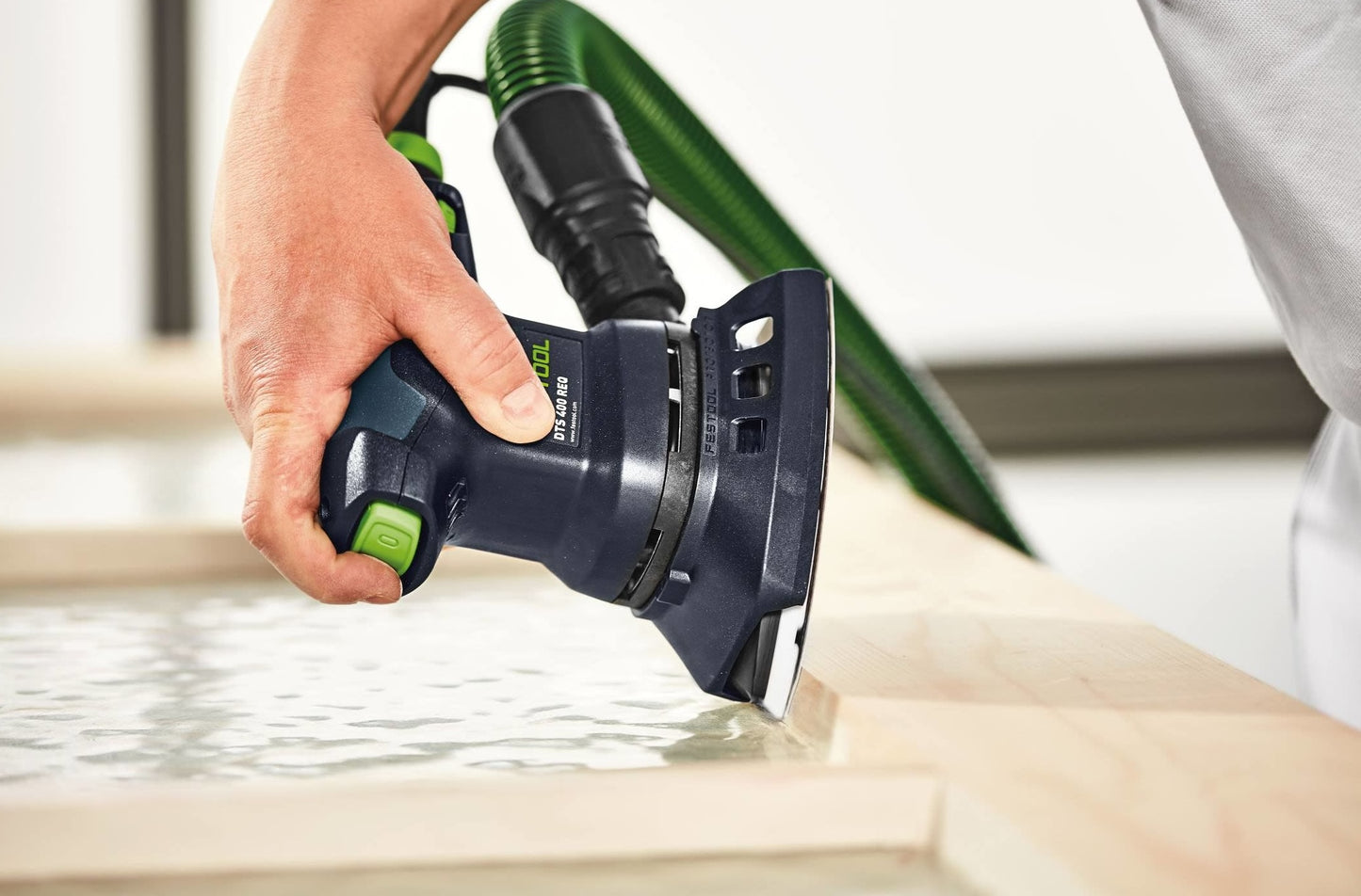 Handheld delta sander with green hose attachment used on wooden surface in woodworking and power tools context