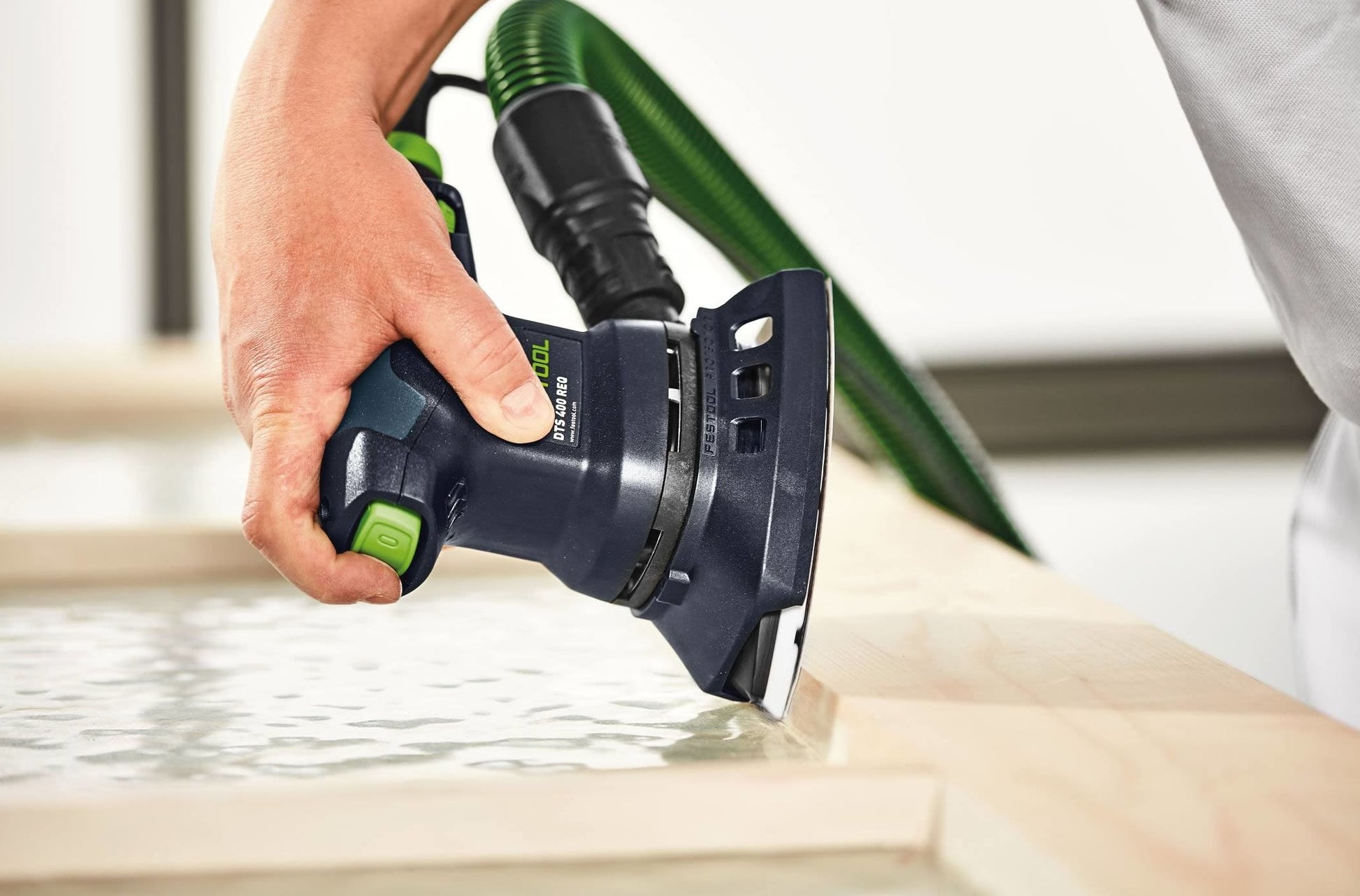 Handheld delta sander with green hose attachment used on wooden surface in woodworking and power tools context