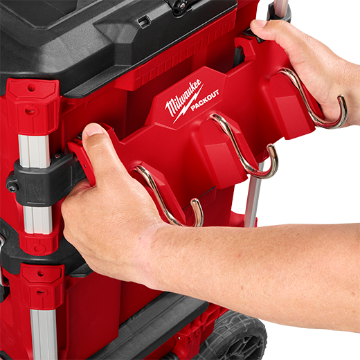 Person attaching red Milwaukee PACKOUT™ 3-hook accessory to modular tool box for workshop storage organization