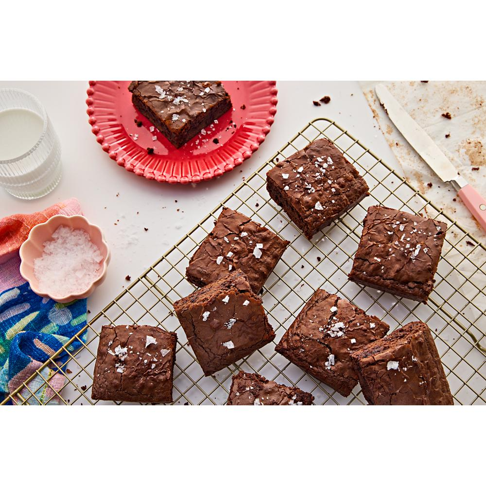 Freshly baked chocolate brownies sprinkled with sea salt cooling on a wire rack beside a glass of milk and pink plate