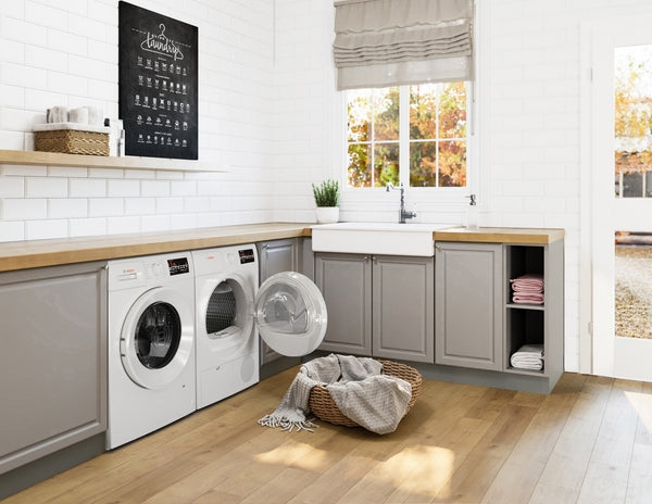 Laundry room with gray cabinets, white Bosch dryer and washer, farmhouse sink, and natural wood countertops with basket on floor