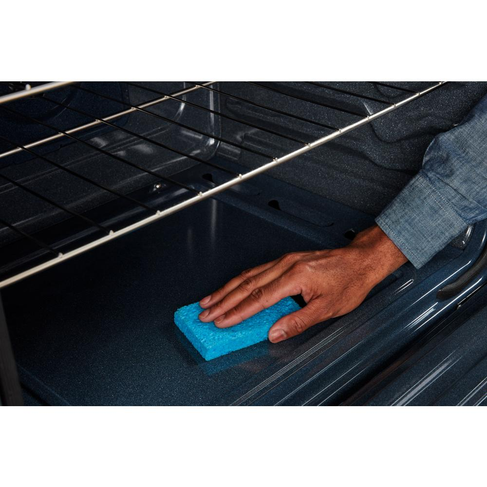 Hand cleaning the interior bottom of a gas range oven with a blue sponge in a kitchen appliance setting