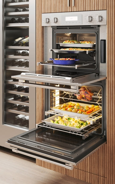 Double steam wall oven with open doors displaying multiple trays of cooked dishes in modern kitchen setting