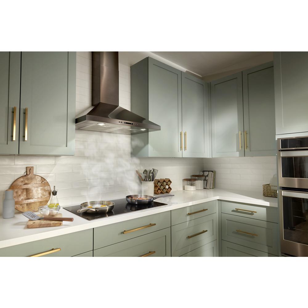 Modern kitchen with green cabinetry, stainless steel chimney wall mount range hood, and built-in oven in appliance setting