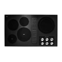 Top-down view of a black electric cooktop featuring multiple circular burners, a central ventilation grate, and a set of silver control knobs on the right side.