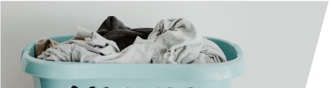 Light blue plastic laundry basket filled with unfolded clothes against a plain light gray background