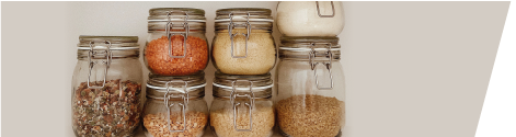 Glass jars with metal clasps filled with various dry goods like spices and grains, arranged neatly against a light background.