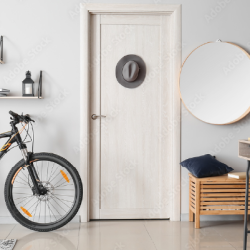 Light-colored wooden interior door with a modern handle, surrounded by a bicycle, wall shelves with decor, a round mirror, and a wooden bench with cushions.