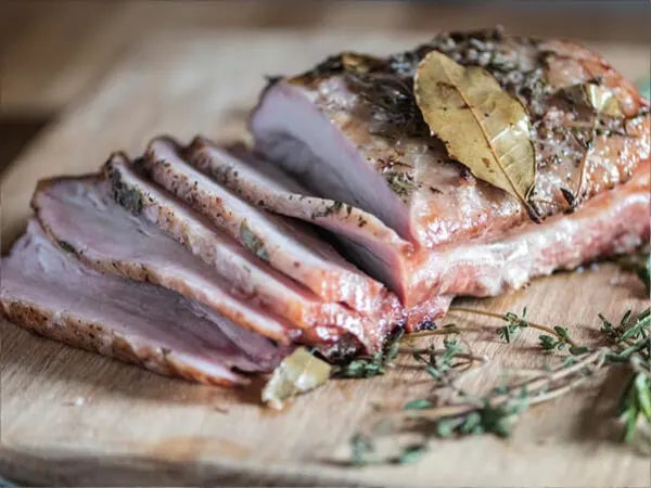 Several slices of herb-crusted cooked meat with bay leaves and fresh thyme on a wooden cutting board