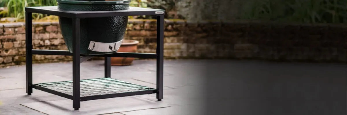 Outdoor charcoal grill with a sleek black metal stand placed on a stone patio, surrounded by a garden and brick wall backdrop.