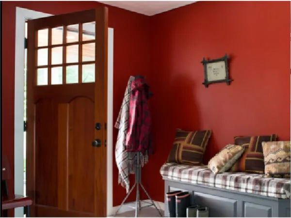 Entryway featuring a wooden door with glass panes, deep red walls, a coat rack with jackets, and a bench with patterned cushions and boots underneath.