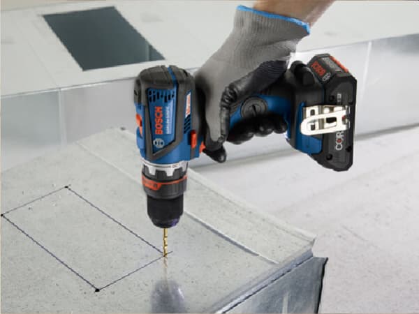 Person wearing a gray glove holds a blue and black cordless drill driver to drill a hole into a metallic surface for home improvement.