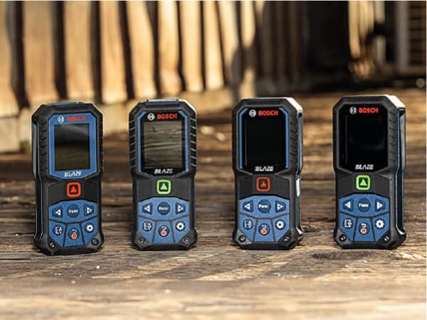 Four handheld Bosch laser measuring devices with digital displays and control buttons are lined up on a wooden surface in natural light.