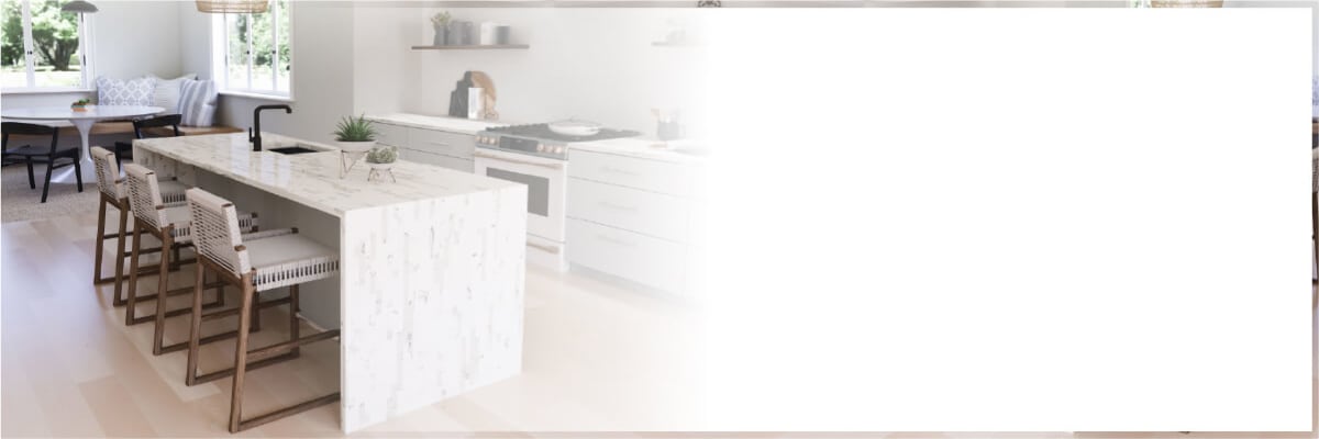 Bright modern kitchen interior featuring a marble island with woven bar stools, white cabinetry, and stainless steel appliances in a home setting.