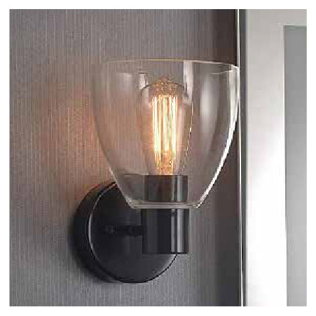 Wall-mounted light fixture with a round black base and a clear glass shade housing an exposed filament bulb against textured gray wallpaper.