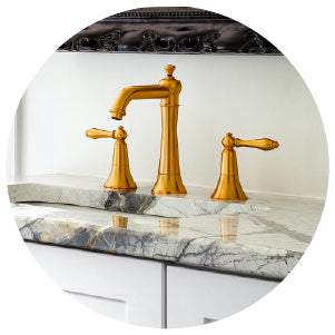 Bathroom sink area with a polished gold faucet set mounted on a marble countertop featuring gray and white veining.