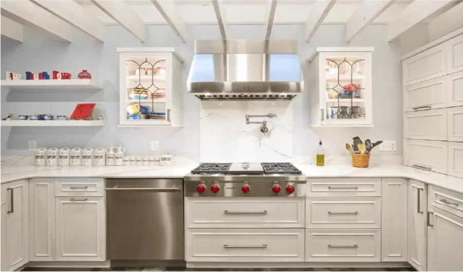 Bright kitchen featuring white cabinetry with stainless steel appliances, decorative glass front cabinets, and a stainless steel range hood above a gas stove.