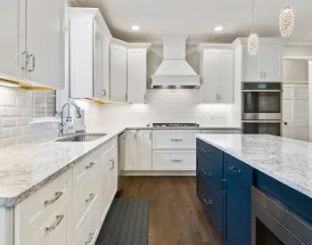 Bright kitchen featuring white shaker-style cabinetry, marble countertops, a blue island with storage drawers, stainless steel appliances, and pendant lighting.