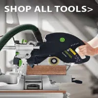 Sliding miter saw with black and green details cutting a wooden board, connected to a green flexible dust extraction hose for cleaner home improvement work.