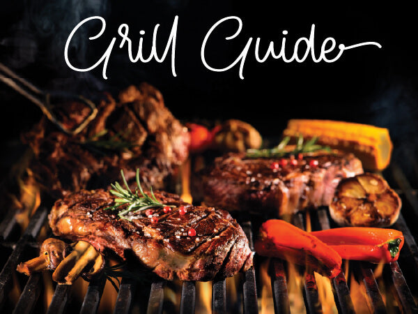 Grill loaded with juicy steaks, red peppers, mushrooms, and herbs cooking over charcoal with smoke rising in a dark setting.