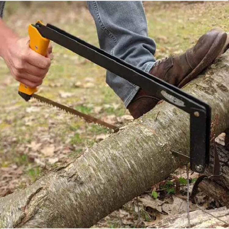 Person wearing brown boots and blue jeans using a hand saw with a yellow handle to cut a fallen tree branch outdoors in a wooded area.