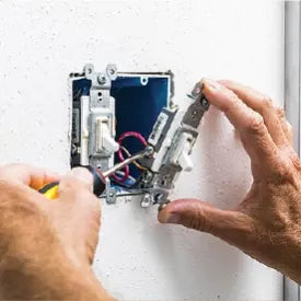 Hands working on installing or repairing an electrical outlet switch with exposed wiring inside a wall during a home improvement task.