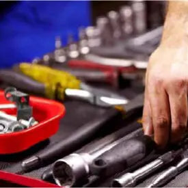 Close-up of a person selecting hand tools from a workbench with various wrenches, pliers, and sockets arranged for home improvement tasks.