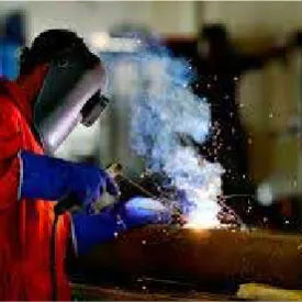 Person wearing protective gloves and a welding helmet using a welding torch to join metal pieces, producing bright sparks and smoke during a home improvement task.