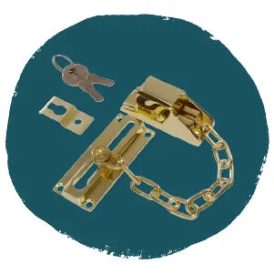 Brass door chain lock with mounting plate, securing chain, and two small keys, displayed on a solid dark teal background.