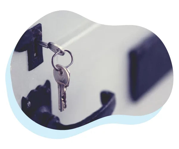 Close-up of a silver key inserted in a white door lock with a blurred dark door handle in the background, suggesting home security or entry.