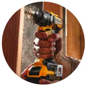 Close-up of a person using a cordless power drill to fasten a screw into a wooden surface, with wood shavings visible in the air.