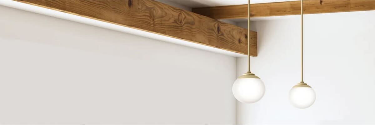 Two modern pendant lights with round white glass shades hanging from thin brass rods against a white wall and exposed wooden ceiling beams.