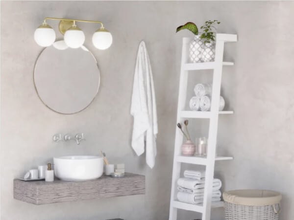 Bathroom vanity area with a round mirror, wall-mounted light fixture featuring three white glass globes, floating sink shelf, and a white ladder shelf holding towels and decor.