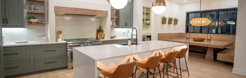 Spacious modern kitchen featuring a large white island with wooden stools, gray cabinetry, stainless steel appliances, and a cozy dining nook with built-in bench seating.