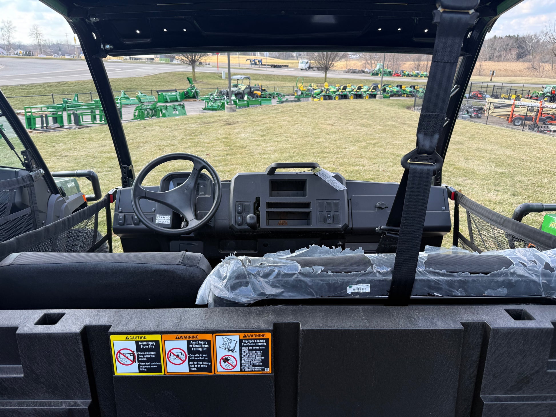 View of the dashboard and seating area inside a John Deere crossover utility vehicle with protective seat coverings in an outdoor equipment lot