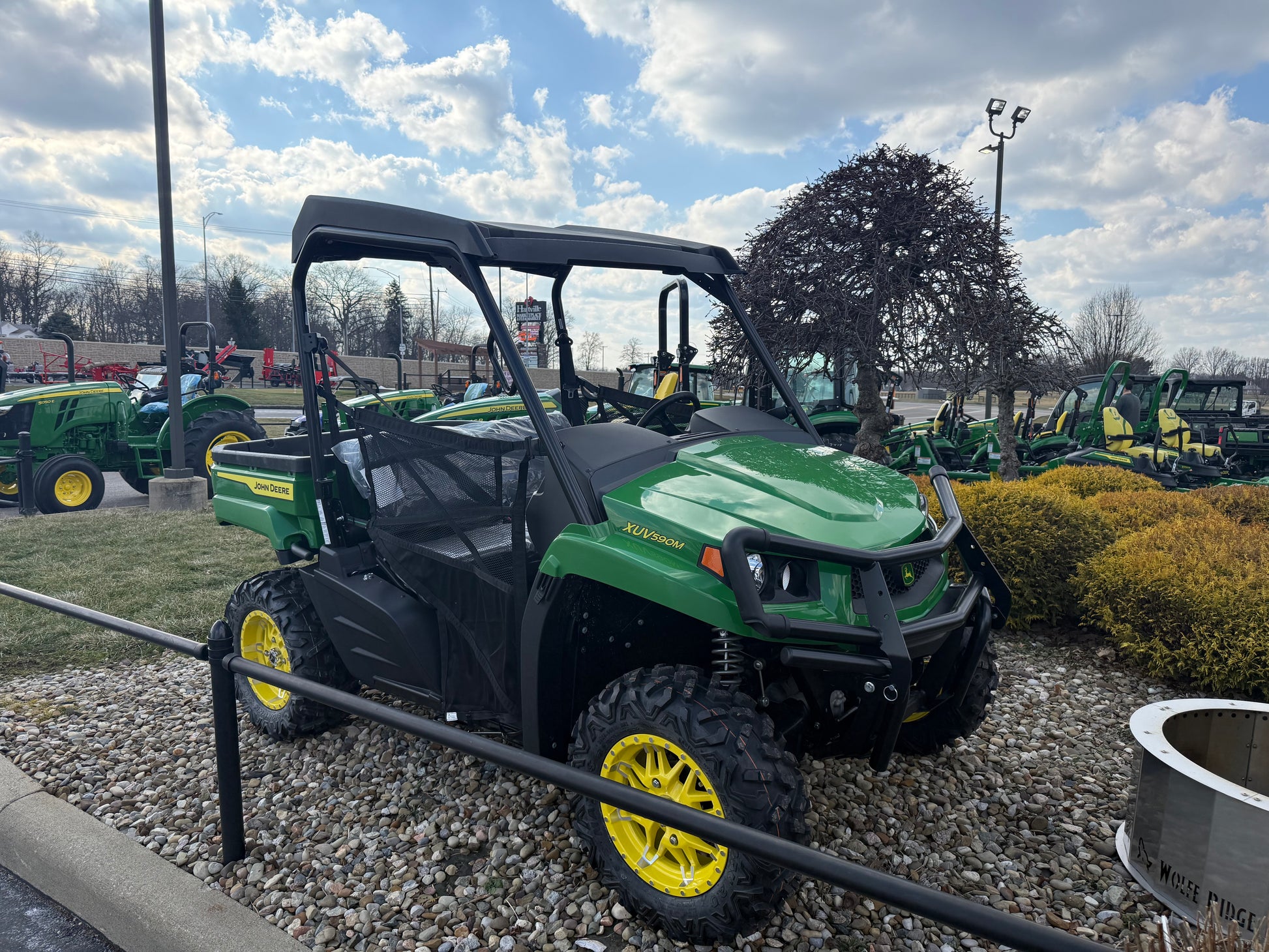 Green John Deere mid-size crossover utility vehicle with yellow wheels and rugged tires, showcased outdoors with other equipment at Hartville Hardware.